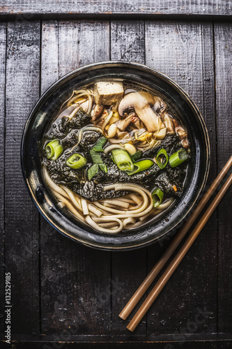 Asian ramen soup with noodles, tofu and nori seaweed in bowl with Chopsticks on dark wooden background.