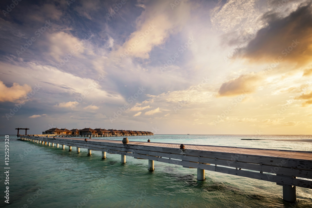 Wooden jetty and water villas. Maldives island resort at sunset