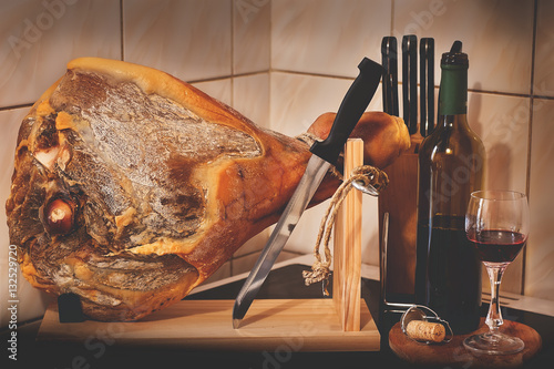 Spanish Jamon Serrano on wooden tabla jamonera with knifes, glass and bottle of red wine. Food photo concept photo