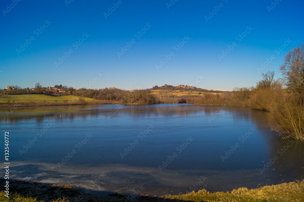 expanse of green grass on the lake with blue sky, countryside and farm around the lake, sunlit water expanse of green grass on the lake with blue sky, countryside and farm around the lake, sunlit water