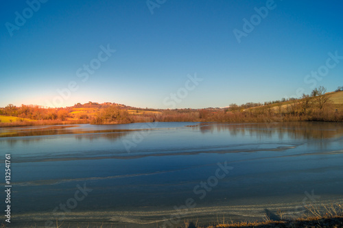 expanse of green grass on the lake with blue sky  countryside and farm around the lake  sunlit water