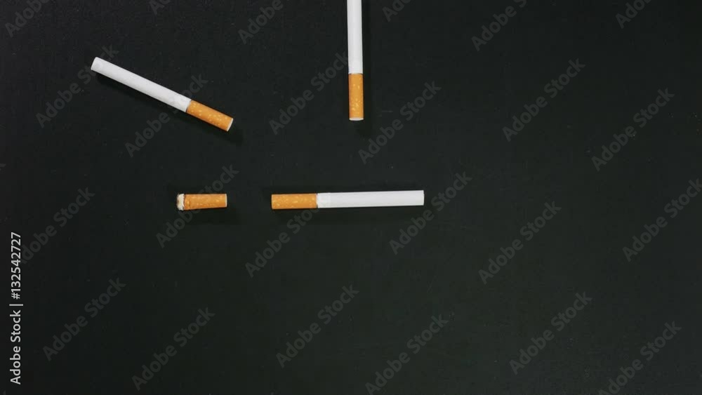 On black surface appear cigarettes one by one and form clock, each one is burned down and disappears until all are gone, smoking. Close up, stop motion, 4K Ultra HD. On black surface appear cigarettes one by one and form clock, each one is burned down and disappears until all are gone, smoking. Close up, stop motion, 4K Ultra HD.