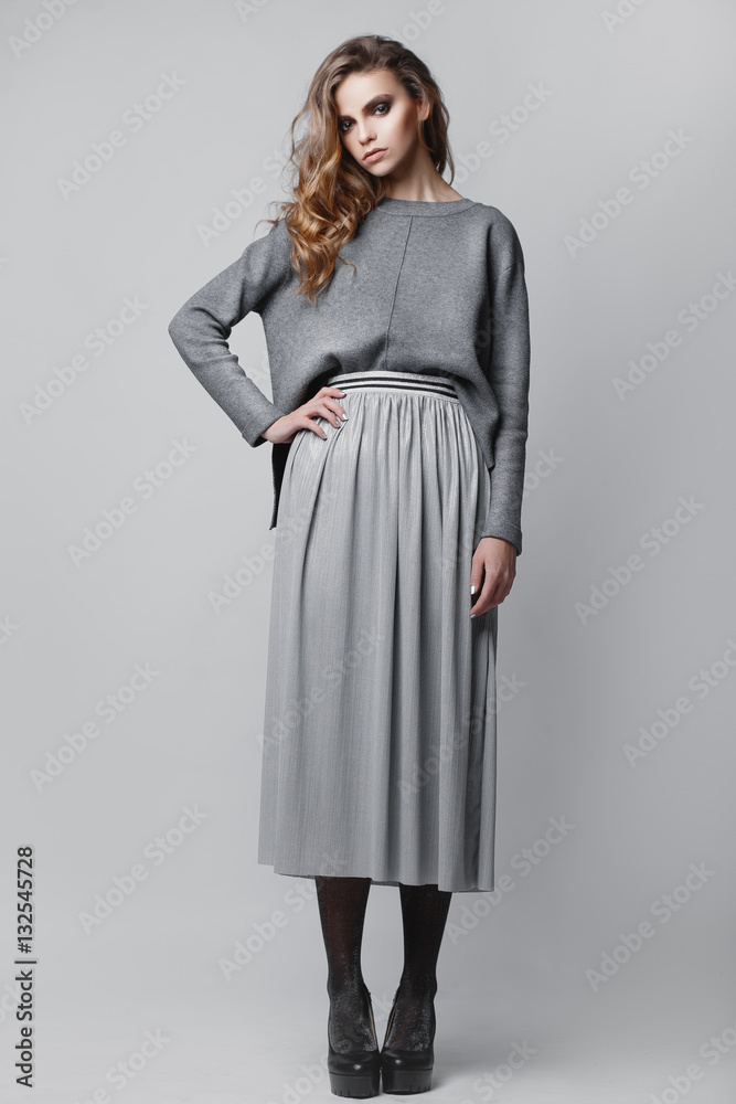 Studio portrait of a full-length stylish young girl in a gray skirt and a gray sweater on a gray background