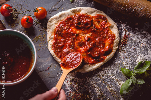 Girl is placing tomato sauce on fresh pizza