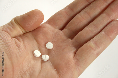 Hand holding 3 white pills, thumb closed