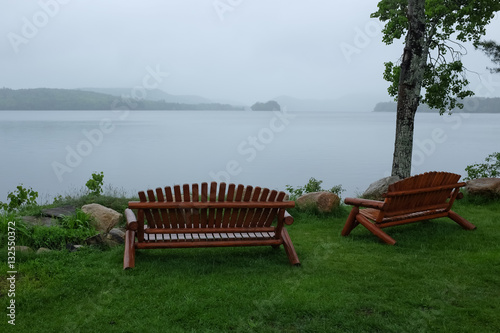 Empty park benches by the lake in the rain.