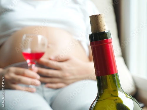 Wine bottle with background of pregnant woman with glass of wine in hand