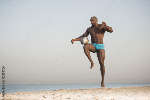 muscular man in blue shorts playing with soccer ball on beach