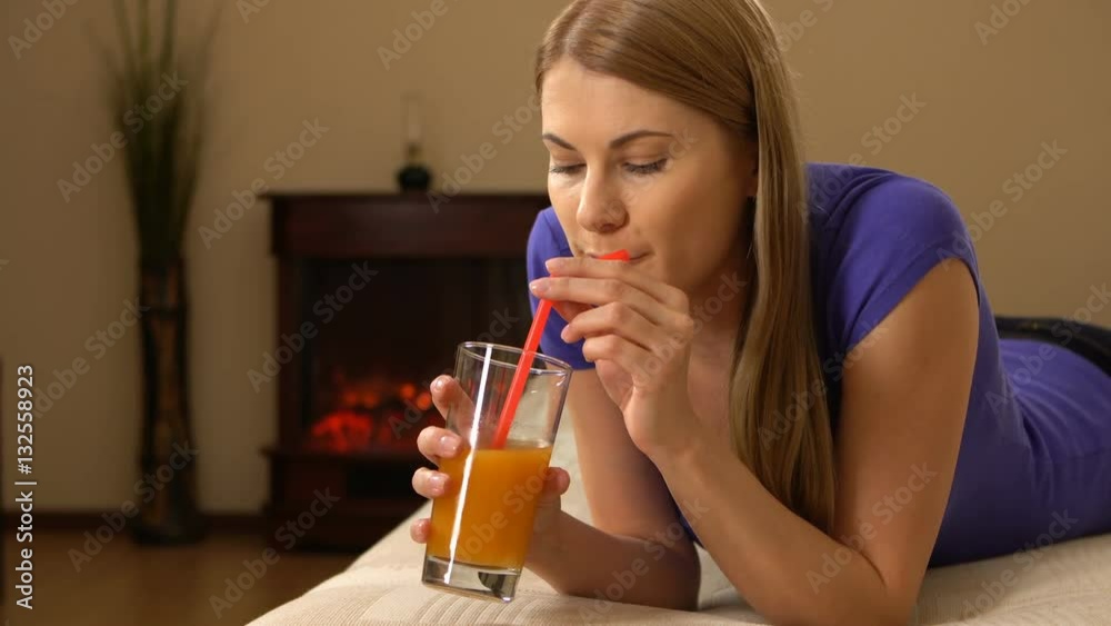 Attractive beautiful young woman lying on a sofa and drinking juice from a glass. Attractive beautiful young woman lying on a sofa and drinking juice from a glass.
