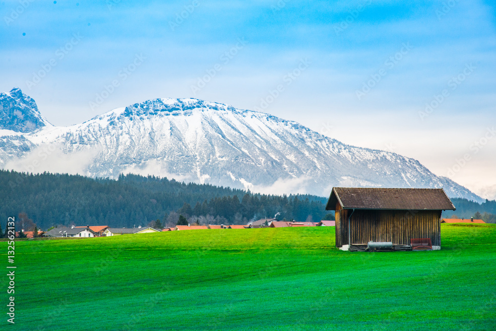 View of fresh green meadows with a house and Alps in the background, Germany - April, 2016