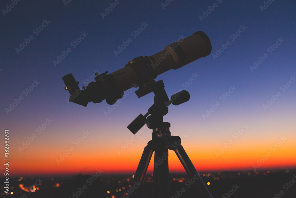 Silhouette of a telescope with de-focused city lights.