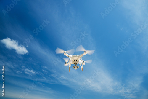 quadrocopter flight from digital camera. white drone hovering in a bright blue sky. New technology in the aero photo shooting. © galaganov