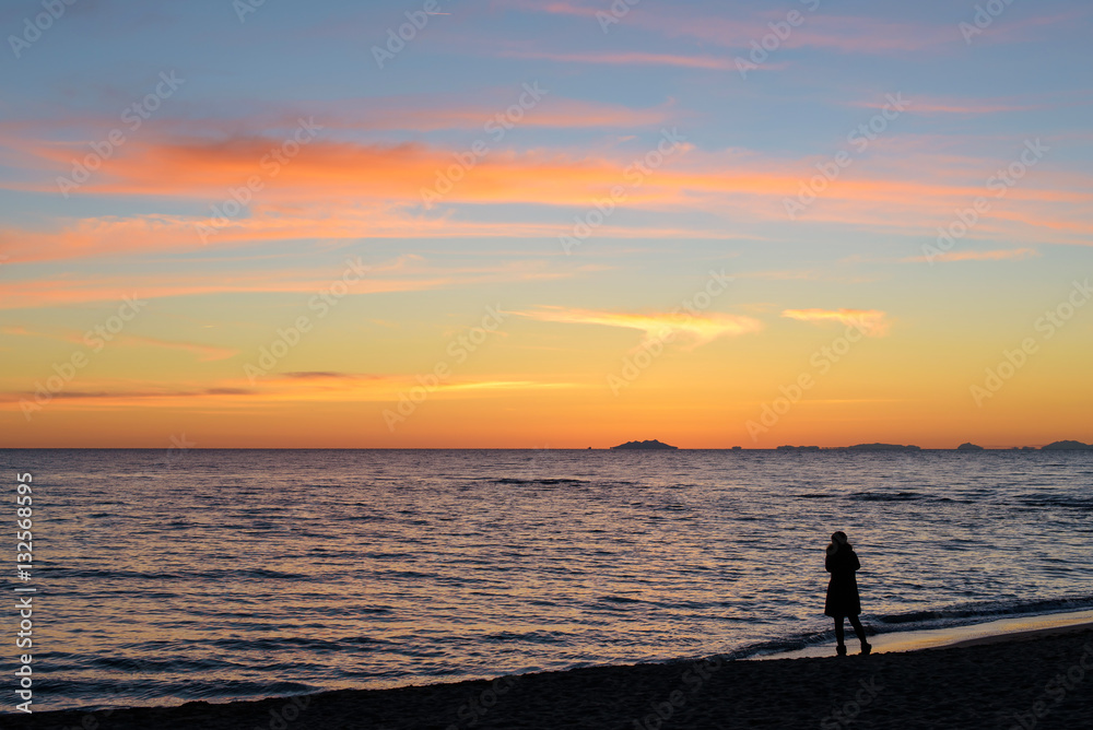 silhouette of woman standing alone on the beach at sunset