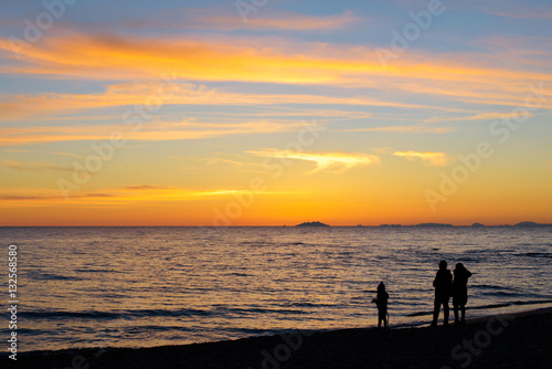silhouette of family standing on the beach watching the sunset © Georgia K