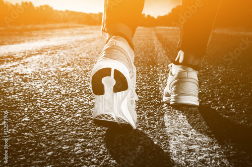 Young athlete in sneakers makes summer morning workout and exercises. Running on the move close-up on a background of the rising sun. Sports and healthy lifestyle.
