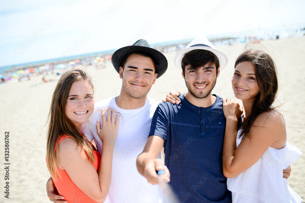 group of four young people making selfie on the beach during summer