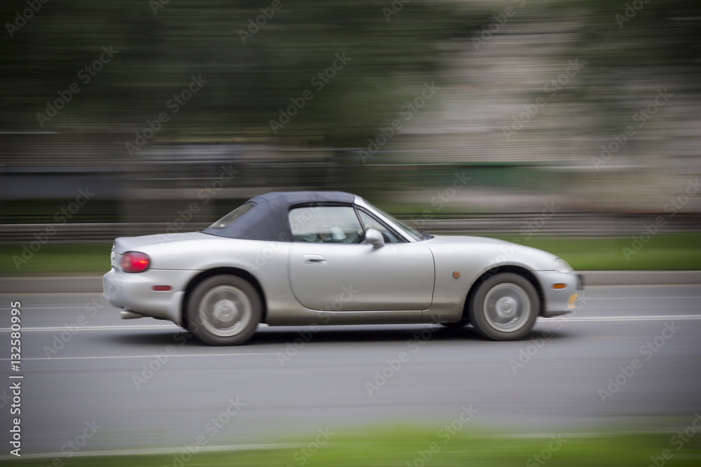 Cabriolet car racing on road. Convertible with a closed top rushing down the road. Everything is blurred.