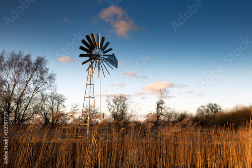 Wind pump with blue sky and farmland in background.