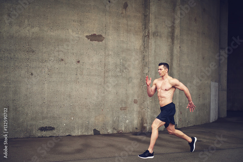 Shirtless young male running against concrete wall