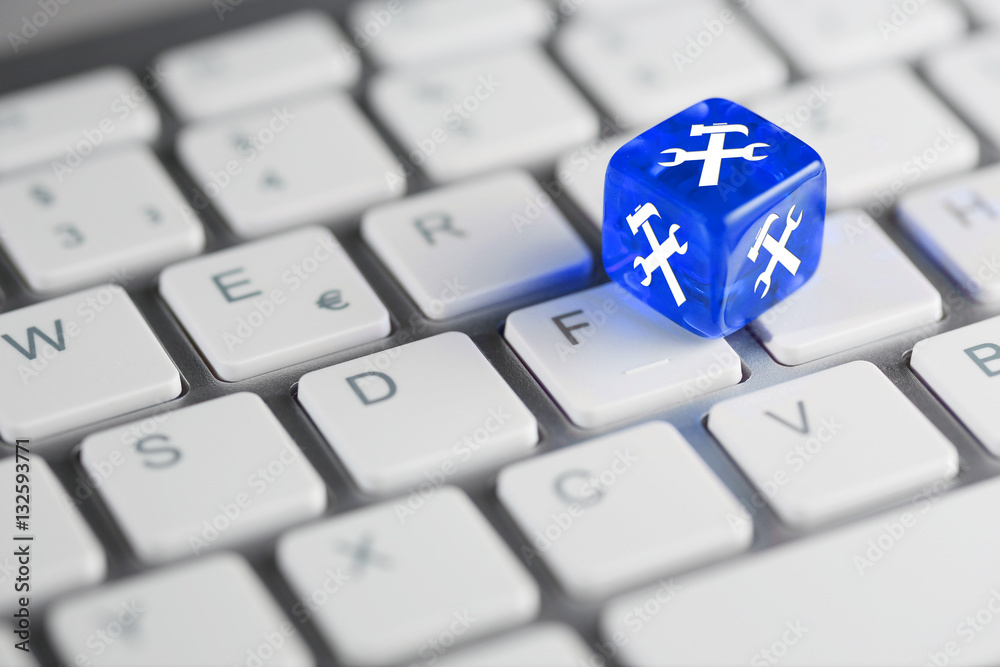 Blau farbener / blauer Würfel mit Hammer und Schraubenschlüssel auf Tastatur