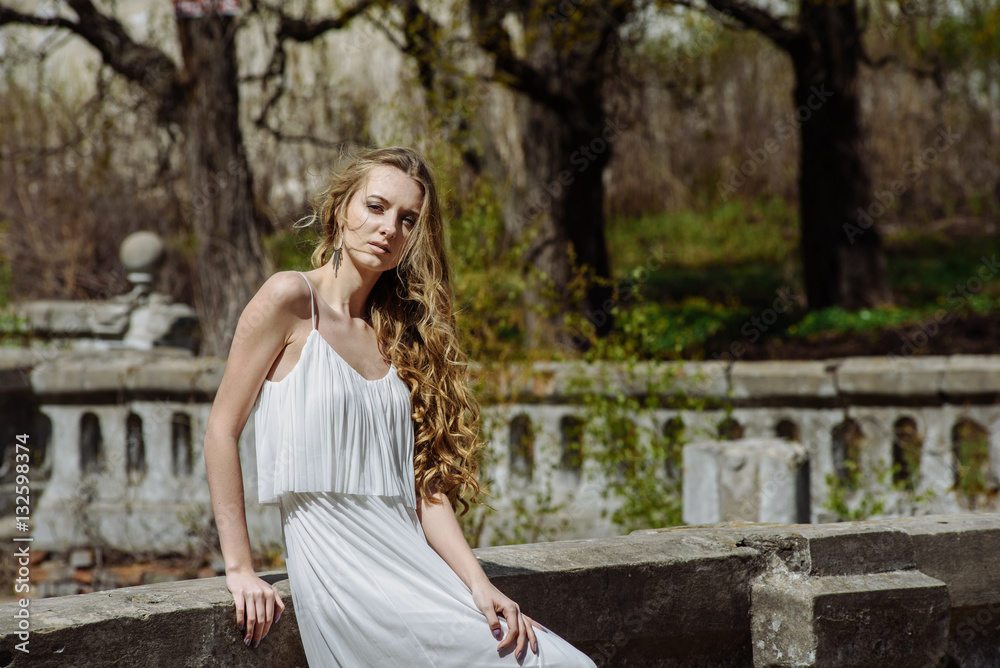 Outdoor summer portrait of young pretty cute girl. Beautiful woman posing at old bridge. in white dess standing near stone railing. Photo has an model. Outdoor summer portrait of young pretty cute girl. Beautiful woman posing at old bridge. in white dess standing near stone railing. Photo has an model.