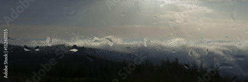 raindrops on a window with view over wooded mountains 