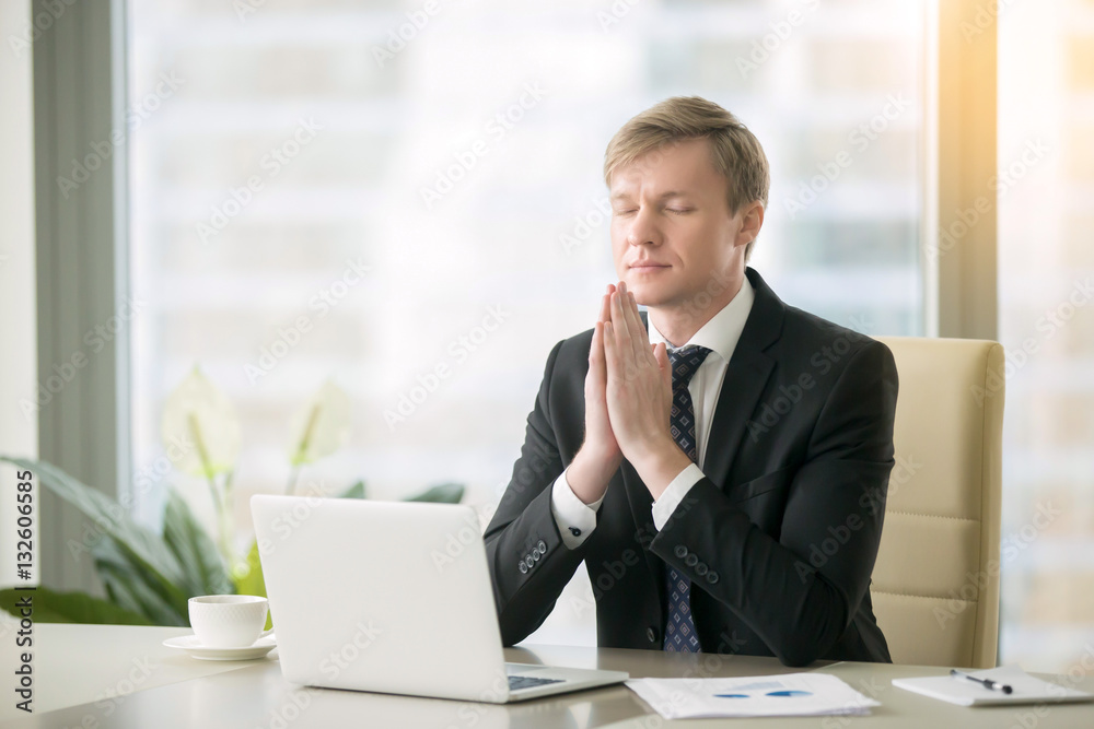 Young businessman working at desk in yoga pose, praying, meditating, relaxing. Stress free work, time for practice, mindfulness and wellbeing, stay healthy on physical, mental emotional level concept Young businessman working at desk in yoga pose, praying, meditating, relaxing. Stress free work, time for practice, mindfulness and wellbeing, stay healthy on physical, mental emotional level concept