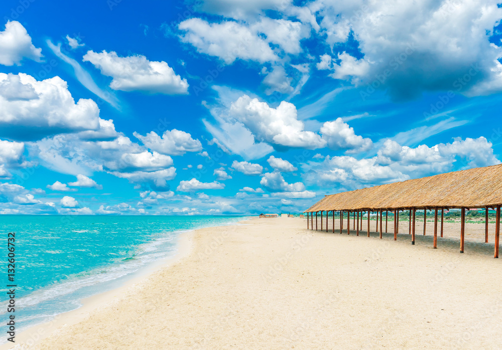 Beautiful tropical sandy beach with canopies from the sun and blue cloudy sky