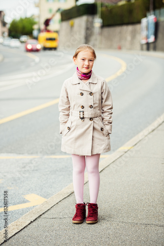 Outdoor portrait of young kid girl wearing beige trenchcoat and red boots