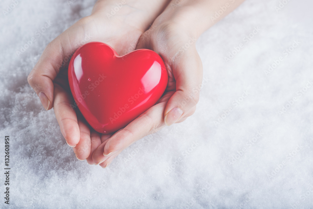 Woman hands are holding a beautiful glossy red heart in a snow b Woman hands are holding a beautiful glossy red heart in a snow b
