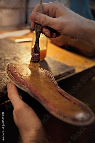 Shoemaker makes shoes for men. He smears special liquid  with a brush.