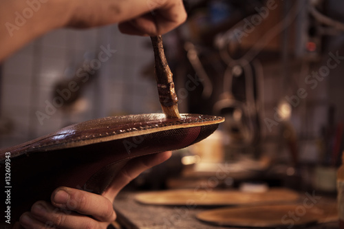 Shoemaker makes shoes for men. He smears special liquid  with a brush.