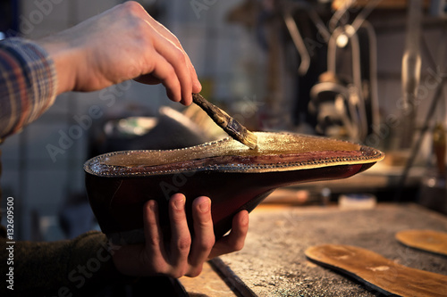 Shoemaker makes shoes for men. He smears special liquid  with a brush. © Kateryna
