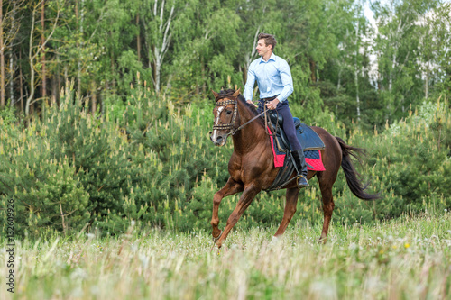 Handsome man riding red horse on a meadow.