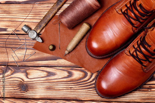 Leather boots and bootmaker tools awl, nails, skien of thread .Wooden background.Concept tools bootmaker.top view. copy space