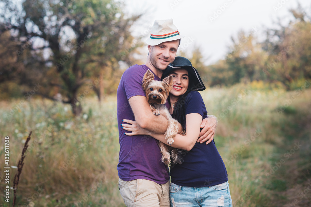 Young couple with little dog yorkshire terrier dressed  t-shirt and hat embracing and have fun on the road,travel, vacation, holidays, vacation, love, life style