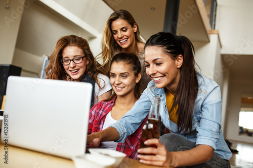 Group of female friends sitting together in living room and watching movie on on laptop.Home party.