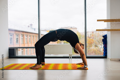 Yoga practice. Man doing bridge pose inside room with panoramic windows.
