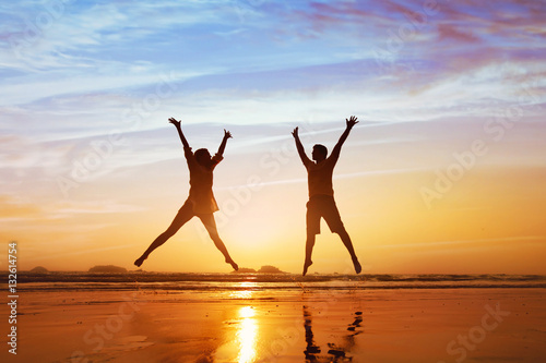 Wall Mural happy couple jumping on the beach at sunset, family summer holidays or honeymoon