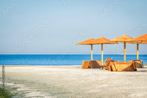 New wooden umbrellas, chair and sunbeds on the beach on a sunny day © elenakirey