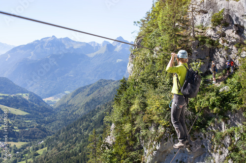 via ferrata climbing, woman in harness crossing rope bridge in the mountains, alpinism or extreme sport