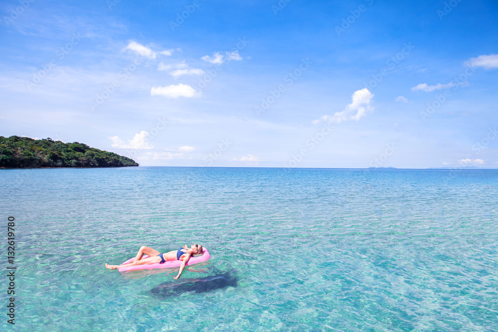woman relaxing on beautiful beach with turquoise water, swimming on inflatable mattress