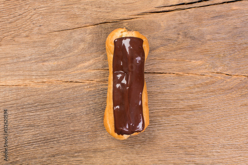 Dessert eclair with chocolate cream on wooden background.