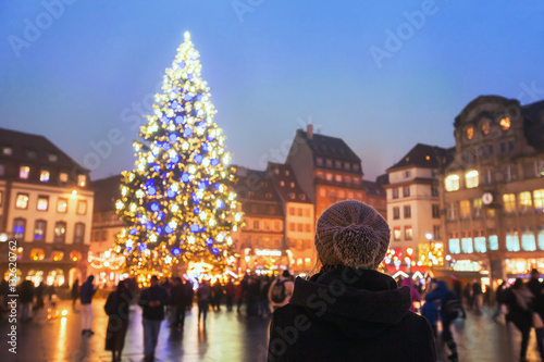 people in christmas market, woman looking at the decorated illuminated tree, festive new year lights in Strasbourg, France, Europe