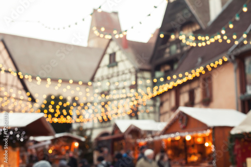 christmas market blurred background  people walking in cozy decorated street with garlandes and wooden houses of shops
