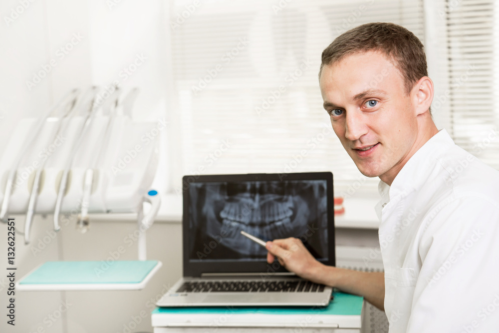 Positive dentist showing on a laptop teeth x-ray picture in dental clinic office. stomatology and health care concept Positive dentist showing on a laptop teeth x-ray picture in dental clinic office. stomatology and health care concept