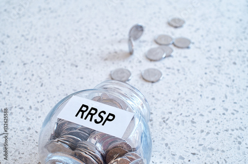 Glass jar with many coins and RRSP word over a marble counter to photo