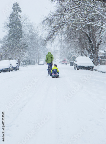Children walk down the center of an empty street dragging sleds in the freshly fallen winter snow.