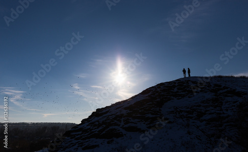 Silhouette of two men standing on the cliff, deep blue sky background
