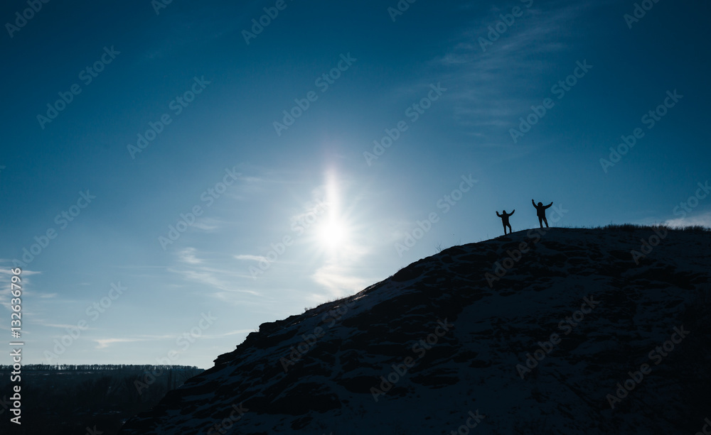 Silhouette of two men standing on the cliff, deep blue sky background
